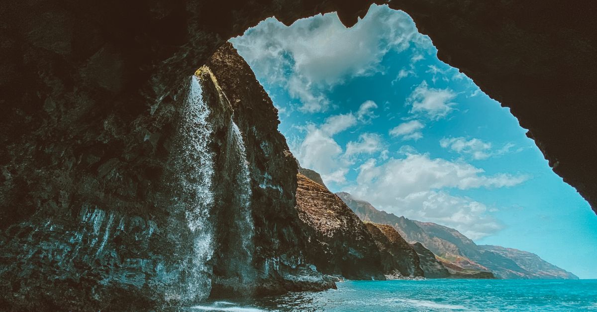 View from inside a sea cave: rock arch framing turquoise ocean and cliffs